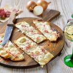 Klassischer Elsässer Flammkuchen mit Zwiebeln und geräuchertem Speck, mit Weißwein serviert – Typical tarte flambée from Alsace with onions and smoked bacon served with Alsatian white wine